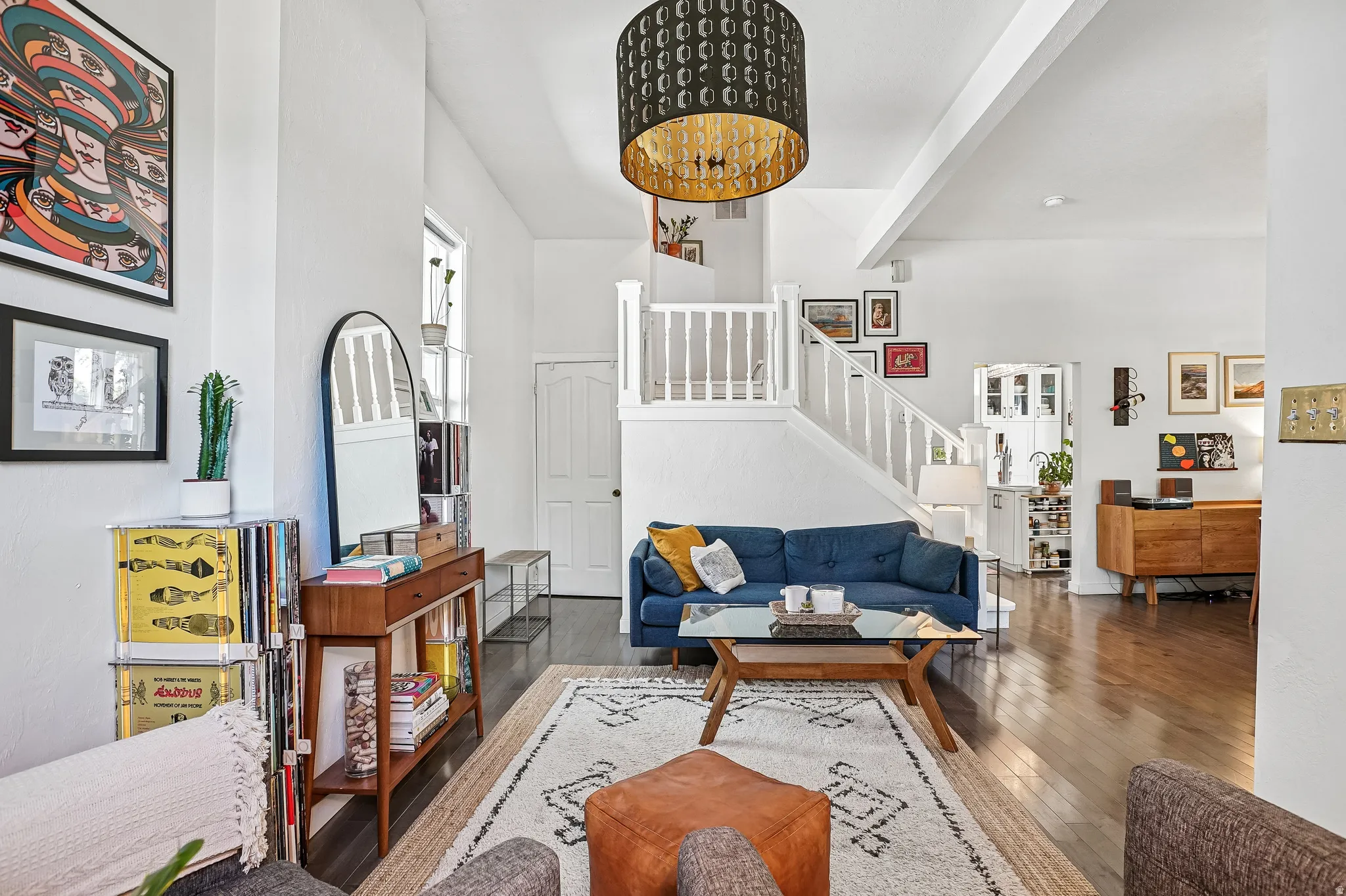Open-concept living area featuring hardwood flooring, a white-painted staircase with banister, and a high-vaulted ceiling
