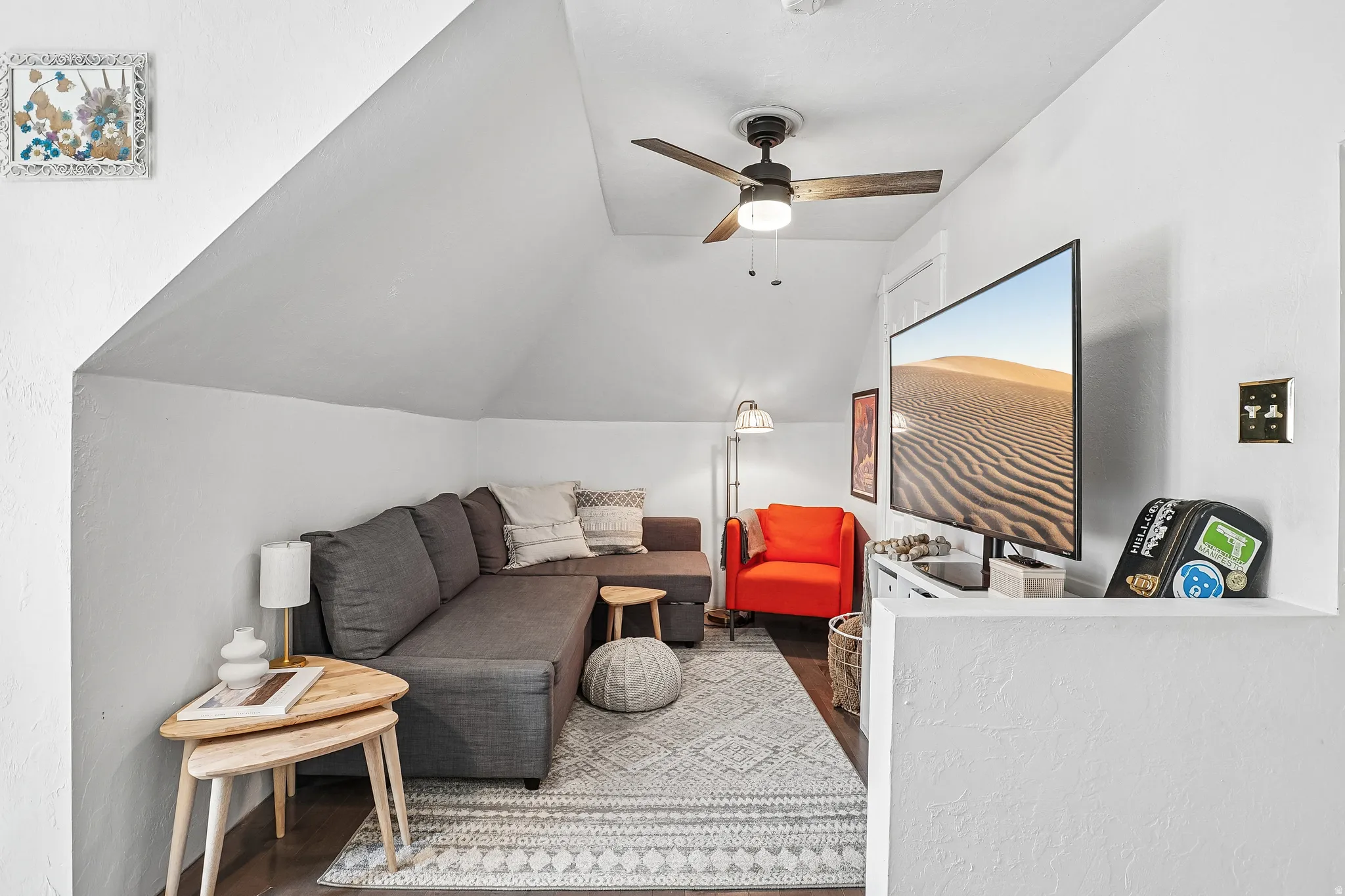 Living area featuring an angled ceiling, dark wood-finish flooring, and a ceiling fan with integrated lighting