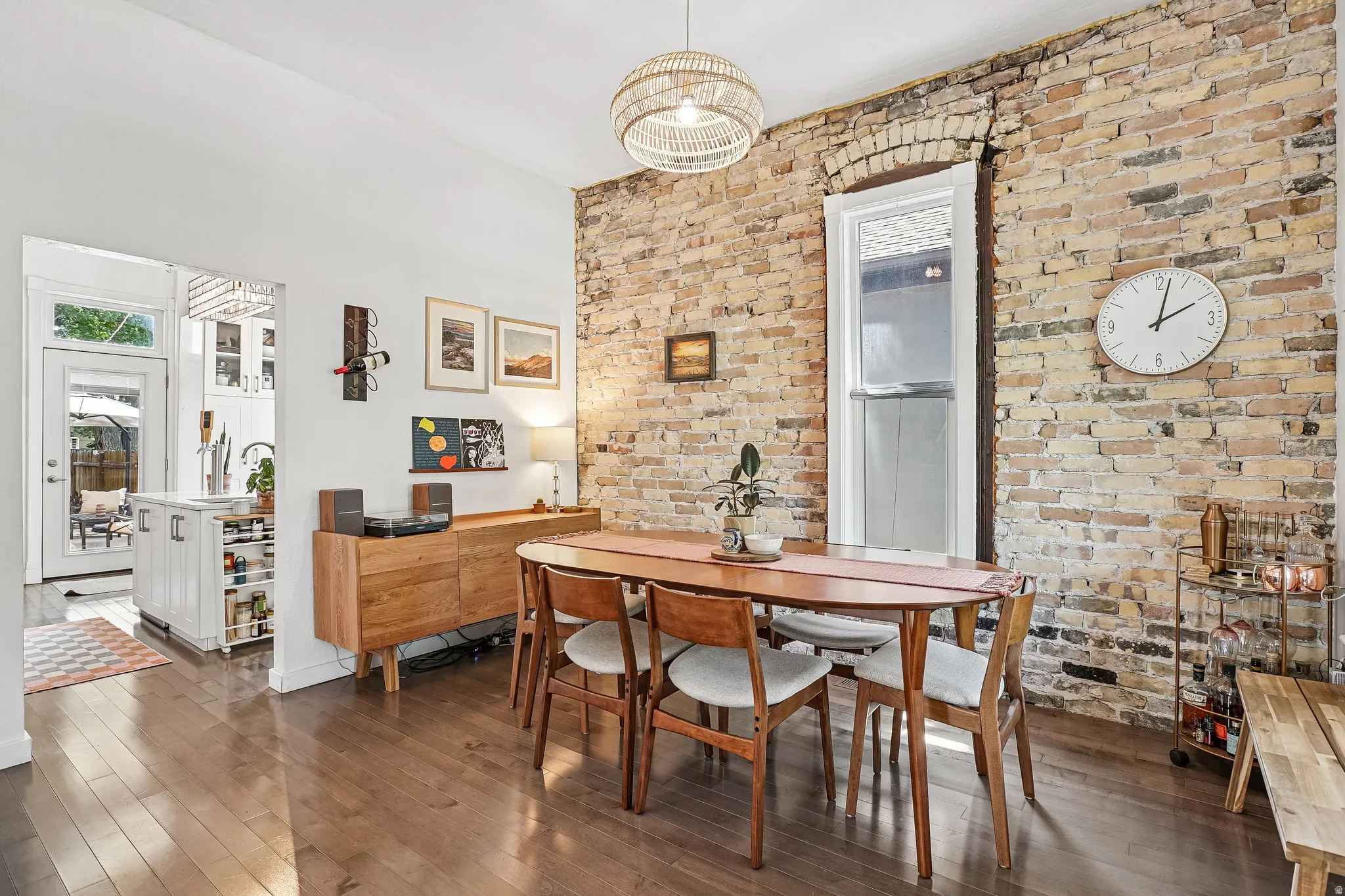 Dining area featuring a prominent exposed brick wall, wood-finish flooring, and a unique woven light fixture