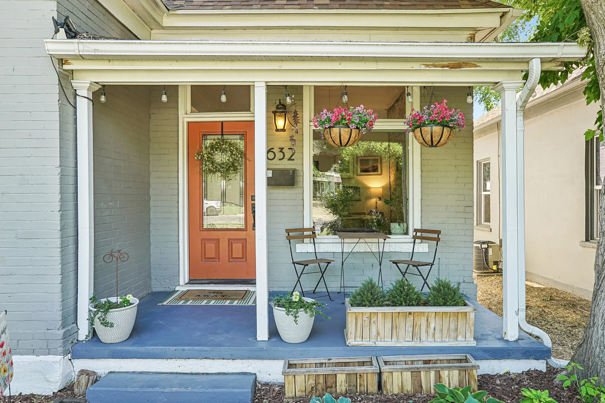 Exterior brick facade with a covered porch featuring an orange entry door, window, and porch lighting