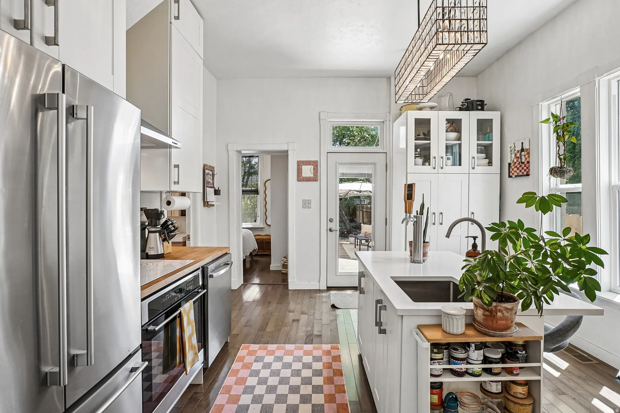 Modern kitchen featuring stainless steel appliances, wood-finish flooring, a central island with an undermount sink, white cabinetry, and abundant natural light from multiple windows and a glass-paneled door