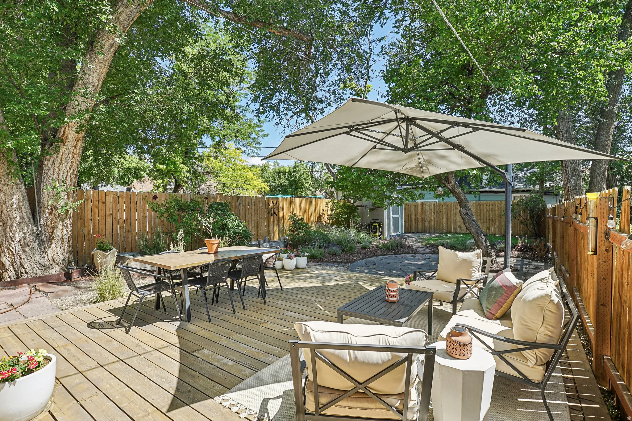 Expansive outdoor deck featuring wood planking, mature trees, and a privacy fence