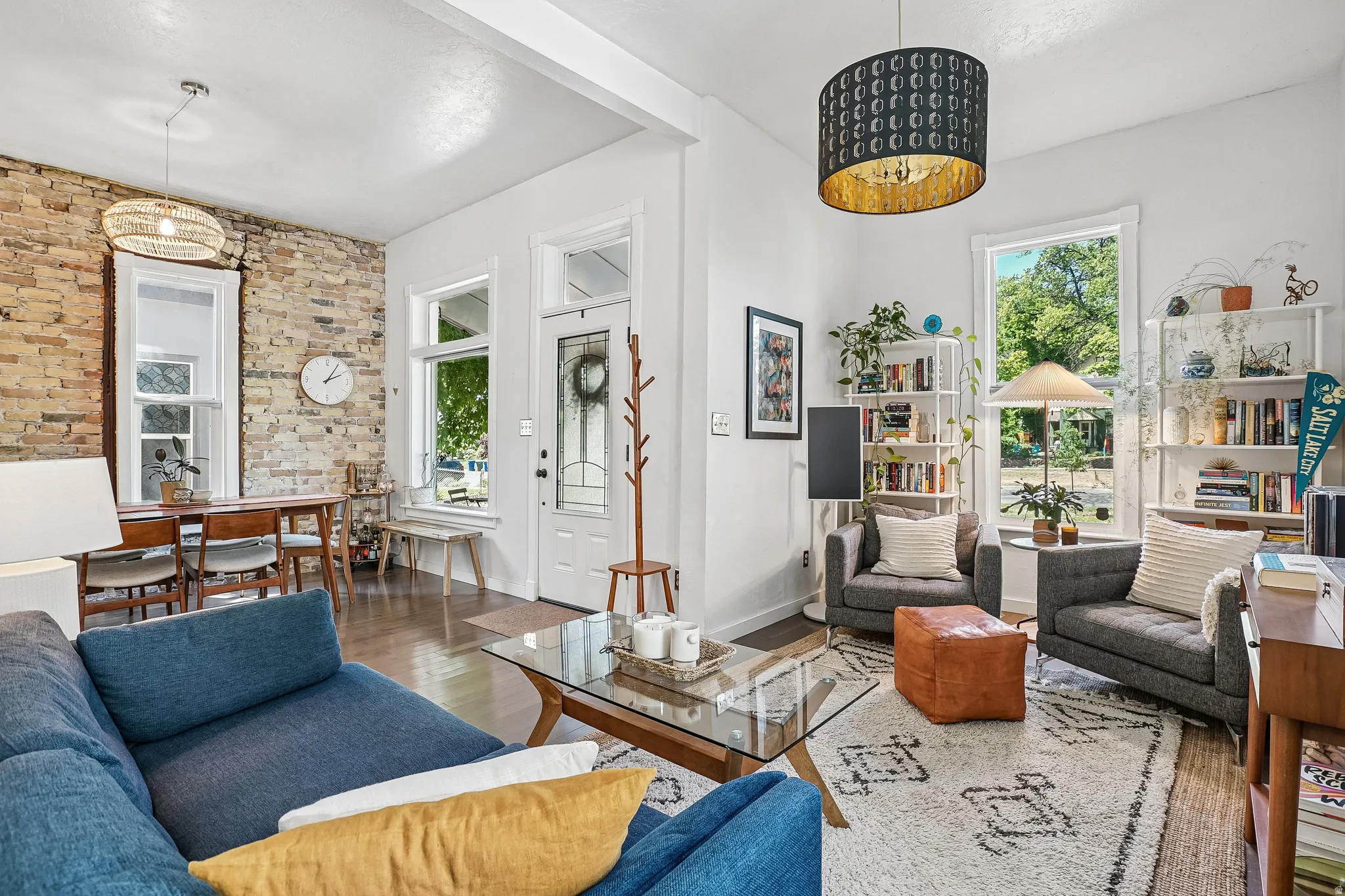 Open concept living area featuring wood-finish flooring, exposed brick accent wall, and multiple large windows