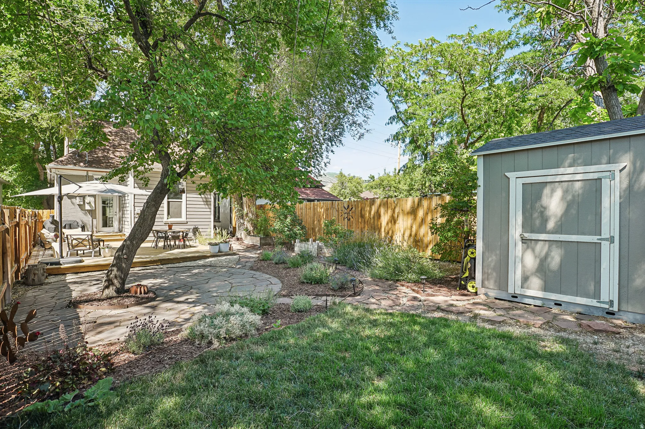 Spacious backyard featuring a manicured lawn, a stone patio, and a raised wood deck
