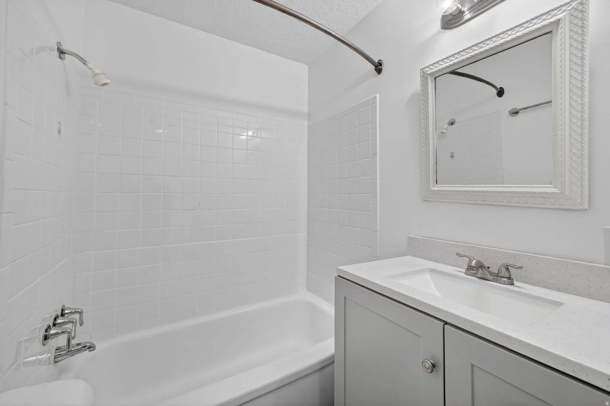Bathroom featuring a tub/shower combination with white tile surround, a single vanity with a light gray cabinet, a white countertop, and a decorative framed mirror