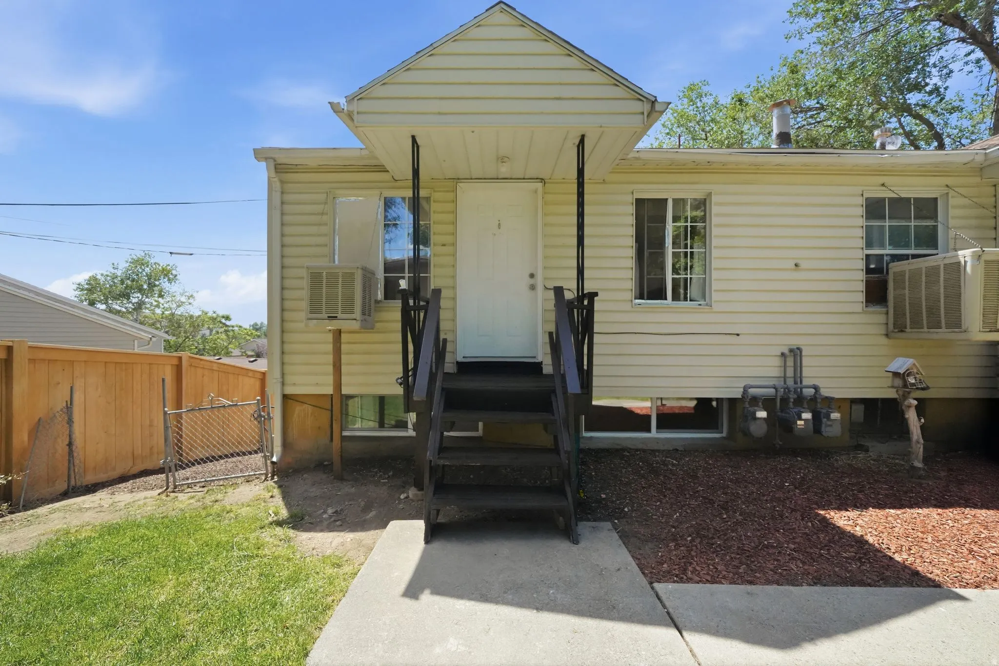 Rear exterior featuring light-colored horizontal siding, a covered entry with dark-stained stairs, and an adjacent wood privacy fence