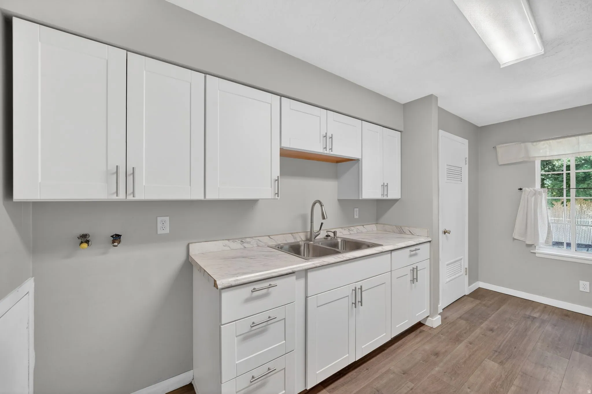 Contemporary white cabinetry with brushed nickel hardware, a stainless steel double sink, and a high-arc faucet