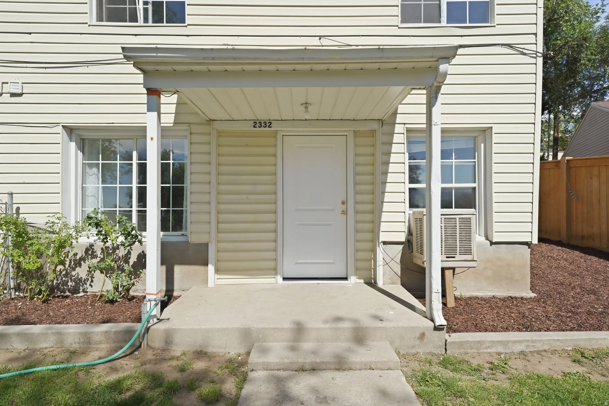 Cream-colored vinyl siding exterior featuring a covered entry, concrete porch, and white paneled front door