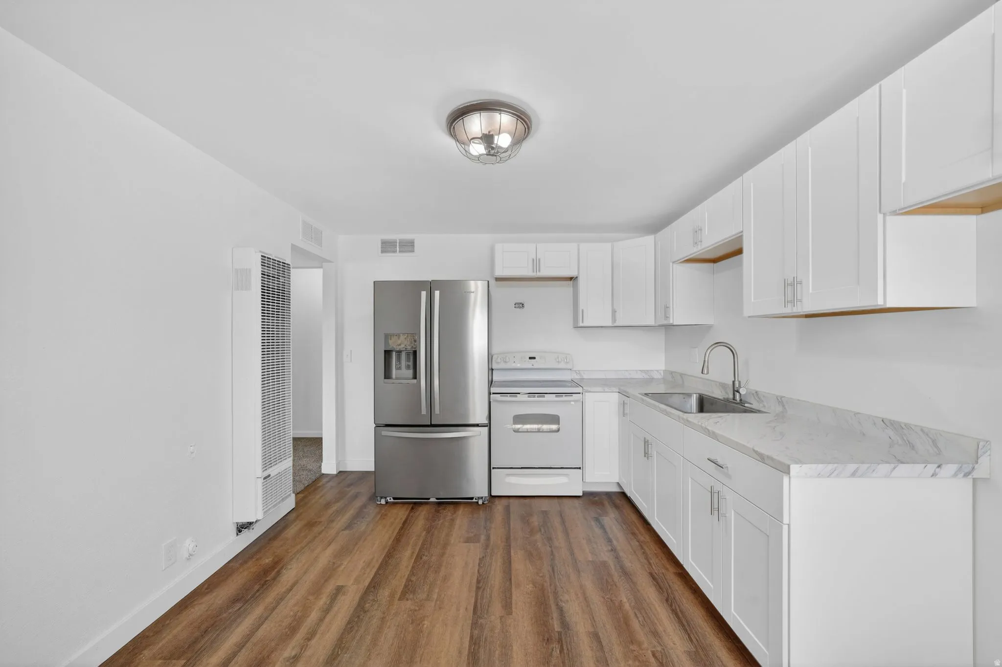 Kitchen featuring extensive white cabinetry, light-toned countertops, a stainless steel refrigerator, and wood-finish flooring