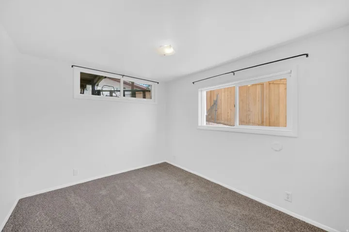 Carpeted room with white walls, featuring two windows with white frames and black curtain rods