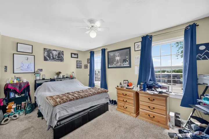 Bedroom featuring neutral wall paint, carpet flooring, a ceiling fan with integrated lighting, and two windows with grids