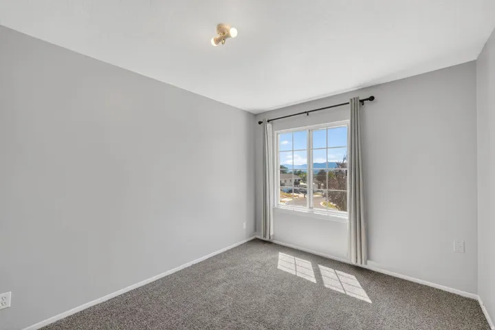 Carpeted room with a multi-pane window, neutral gray walls, and an overhead track light