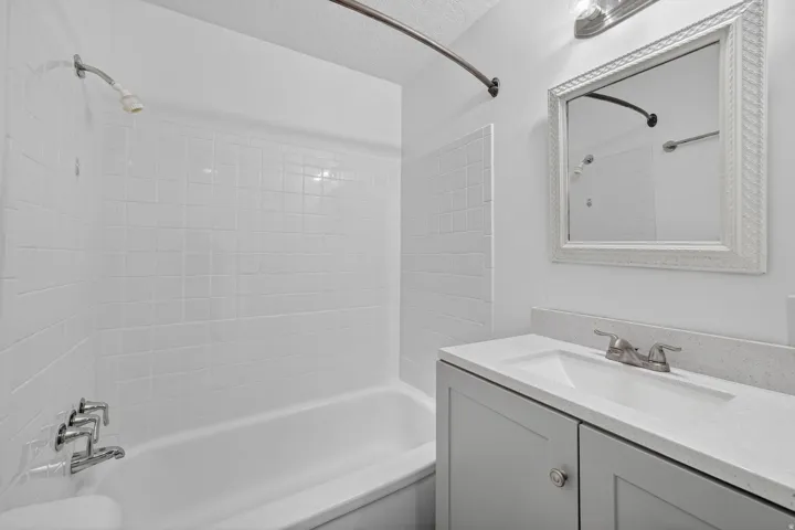 Bathroom featuring a tub/shower combination with white tile surround, a single vanity with a light gray cabinet, a white countertop, and a decorative framed mirror