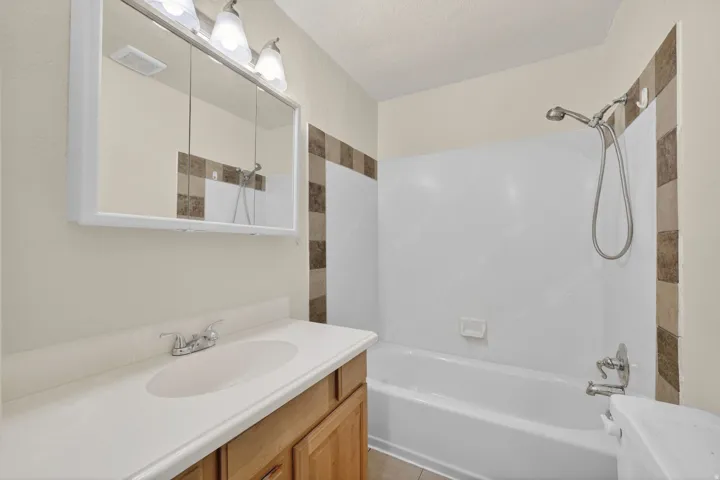 Bathroom featuring a single vanity with a laminate countertop, chrome faucet, and wood-finish cabinetry