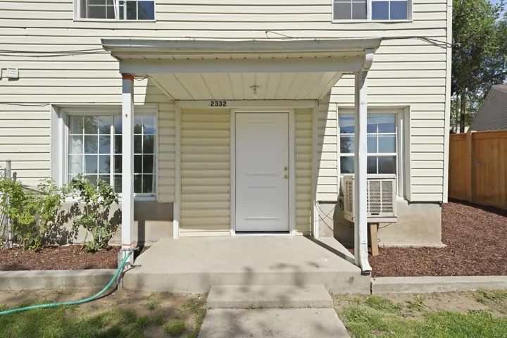 Cream-colored vinyl siding exterior featuring a covered entry, concrete porch, and white paneled front door