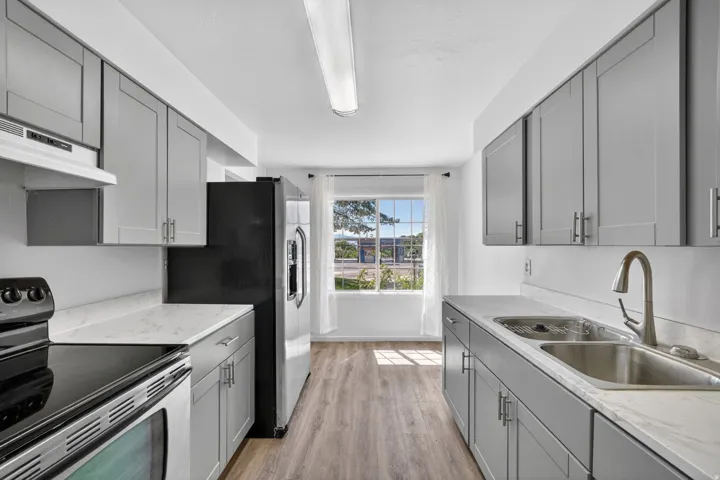 Kitchen featuring grey cabinetry, white countertops, wood-finish flooring, a stainless steel sink with a gooseneck faucet, and a window providing natural illumination
