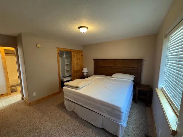 Carpeted room featuring a wooden headboard, a window with blinds, and a built-in closet with wooden sliding doors and shelving
