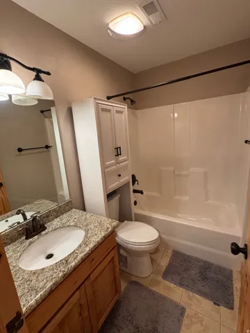 Bathroom featuring a wood-finish vanity with a light-colored countertop, oval sink, and bronze-finish faucet