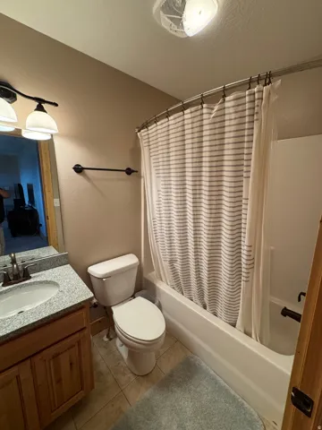 Bathroom featuring a tub and shower combination with a curved rod, a vanity with a light-colored speckled countertop, a white oval undermount sink, and a two-door wood-finish cabinet