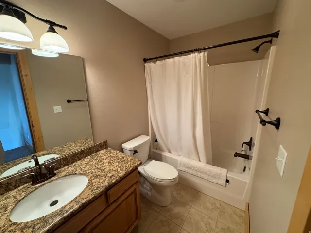 Full bathroom featuring a single vanity with a granite-style countertop, an oval undermount sink, and a bronze faucet