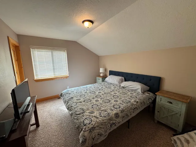 Carpeted bedroom with a slanted ceiling and a window featuring horizontal blinds
