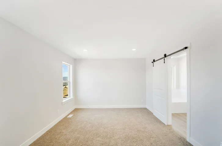 Photos are of a previously built home of the same floor plan. Finishes, colors, features, and upgrades may vary. Carpeted room with recessed lighting, a single window, and a white barn door on a black metal track, opening to a space with wood-finish floor