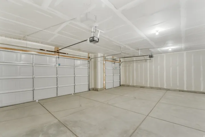 Photos are of a previously built home of the same floor plan. Finishes, colors, features, and upgrades may vary. Spacious garage featuring two overhead doors, concrete flooring with expansion joints, and overhead lighting