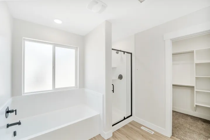 Photos are of a previously built home of the same floor plan. Finishes, colors, features, and upgrades may vary. Modern bathroom featuring a white soaking tub with matte black fixtures, a walk-in shower with a black-framed glass enclosure, and wood-finish