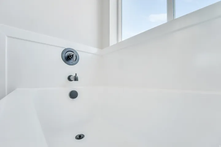 Photos are of a previously built home of the same floor plan. Finishes, colors, features, and upgrades may vary. White alcove bathtub featuring matte black fixtures, a wall-mounted faucet, and a large window providing natural illumination