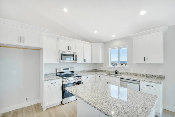 Photos are of a previously built home of the same floor plan. Finishes, colors, features, and upgrades may vary.Modern kitchen featuring white cabinetry, light-toned granite countertops, stainless steel appliances, a black faucet, and wood-finish floorin