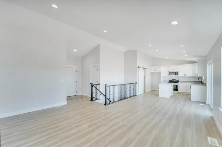 Photos are of a previously built home of the same floor plan. Finishes, colors, features, and upgrades may vary. Open concept living area featuring light wood-finish flooring, vaulted ceilings with recessed lighting, and a modern kitchen with white cabine