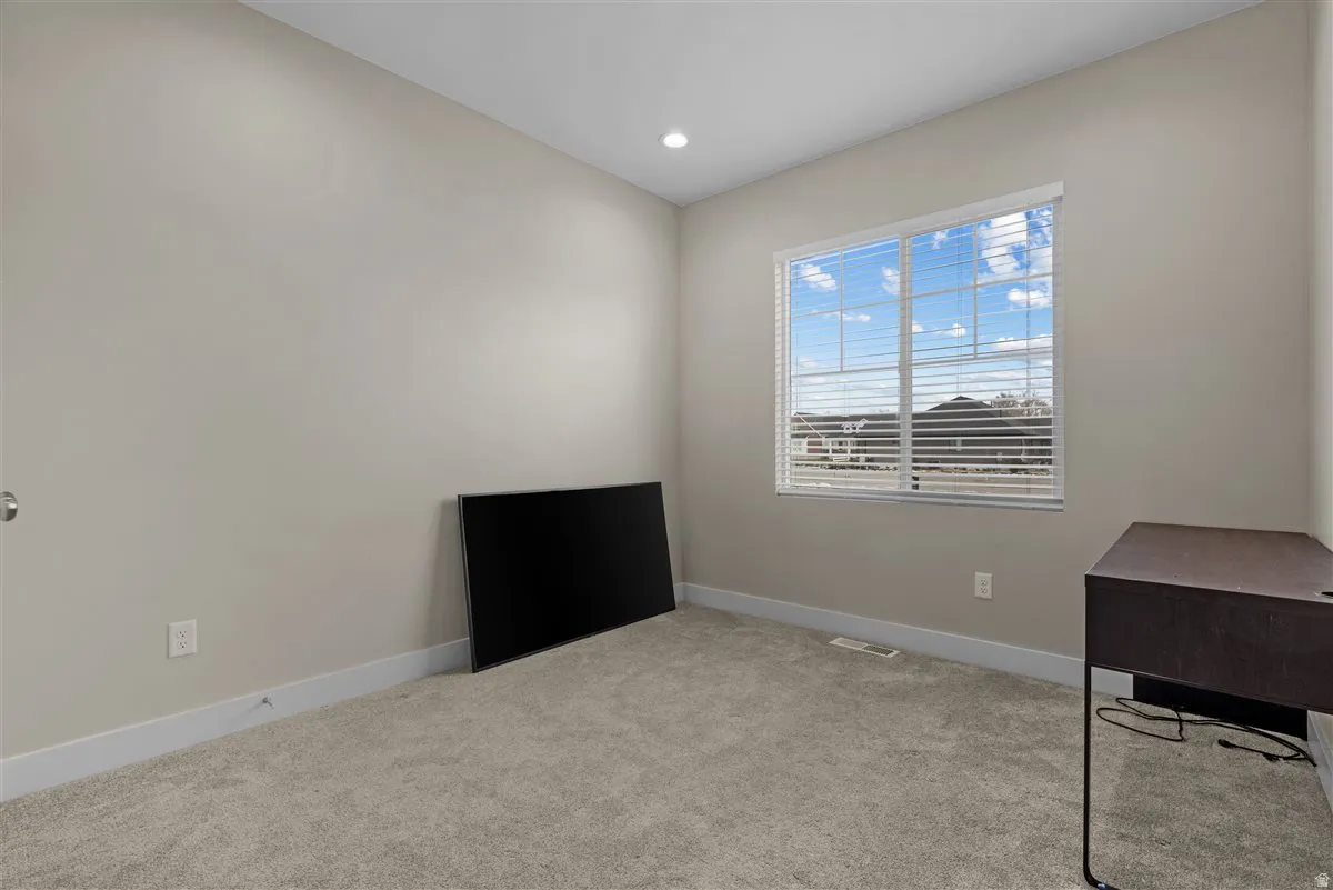 Bright room featuring neutral wall paint, light-toned carpet, a large window with blinds, recessed ceiling lighting, and white baseboards
