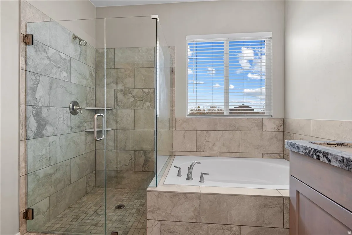 Tiled shower with glass enclosure, separate soaking tub, and window with blinds