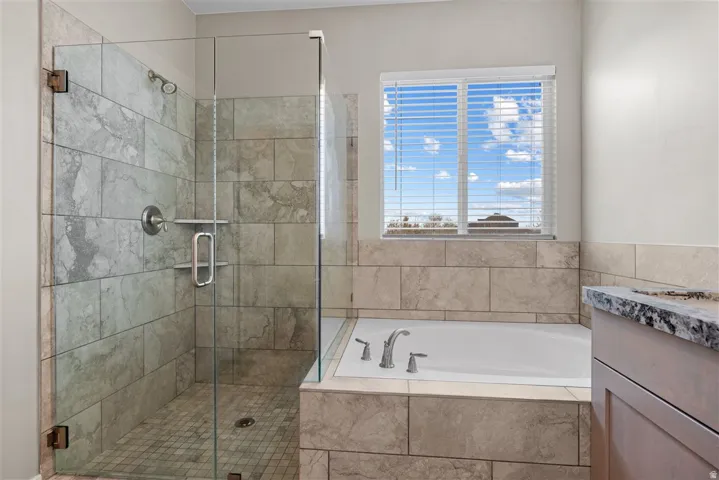 Tiled shower with glass enclosure, separate soaking tub, and window with blinds