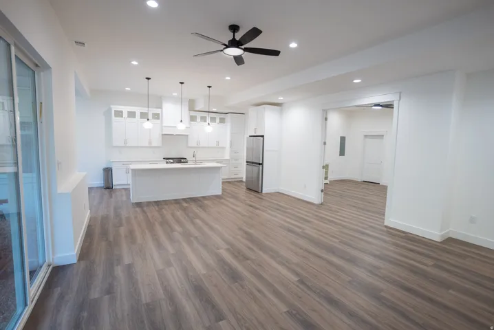 Spacious interior featuring wood-finish flooring, a contemporary kitchen, white shaker cabinetry, stainless steel appliances, and a large center island