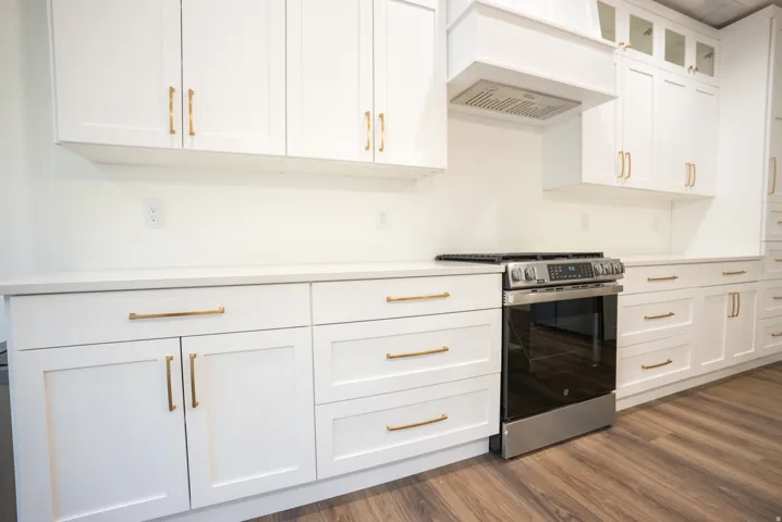 Kitchen featuring white shaker-style cabinetry with gold-tone hardware, white countertops, a stainless steel range, and wood-finish flooring