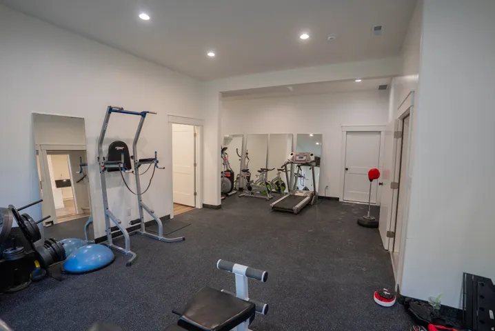 Dedicated fitness space featuring rubberized flooring, recessed lighting, white walls, and multiple door openings