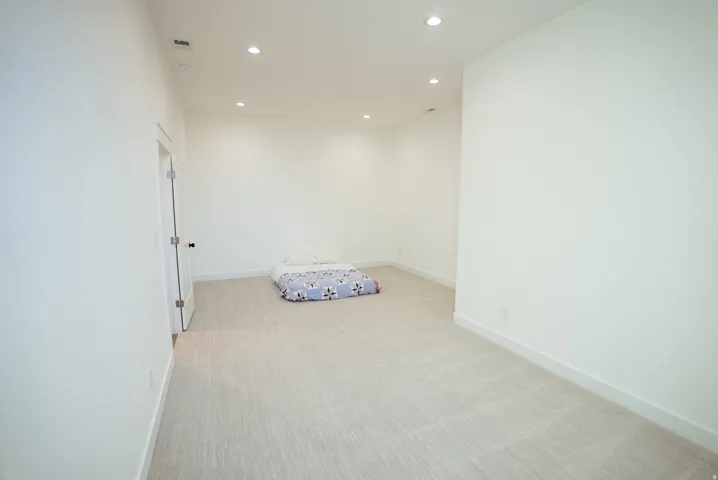 Expansive room featuring light-toned carpet, recessed lighting, white walls, and a white interior door with black hardware