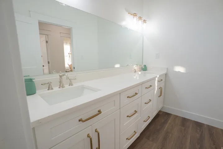 White shaker-style vanity with brass hardware, a light-toned countertop, and an undermount sink with a brushed nickel faucet