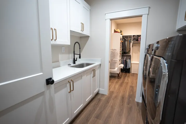 Laundry area featuring white cabinetry with gold-tone hardware, a stainless steel sink with a black pull-down faucet, and wood-finish flooring