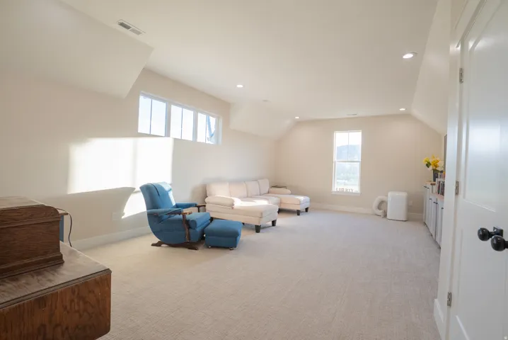 Spacious room featuring vaulted ceilings, light neutral wall tones, recessed lighting, and soft carpeting