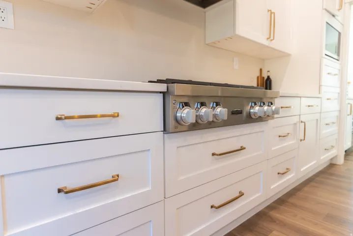 White shaker cabinetry with brass hardware, a stainless steel range, light-toned countertops, and wood-finish flooring