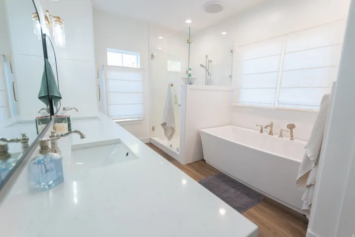Modern bathroom featuring a freestanding tub, glass-enclosed shower, dual vanity with undermount sinks, and wood-finish flooring