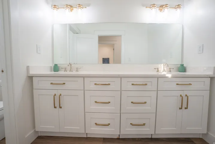 Dual vanity with white cabinetry, gold-tone hardware, and light-toned countertops