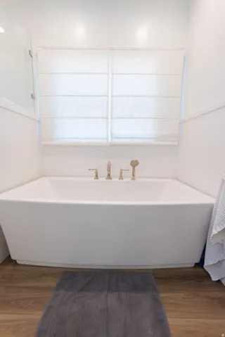 Freestanding soaking tub with polished brass fixtures, surrounded by white wainscoting and wood-finish flooring