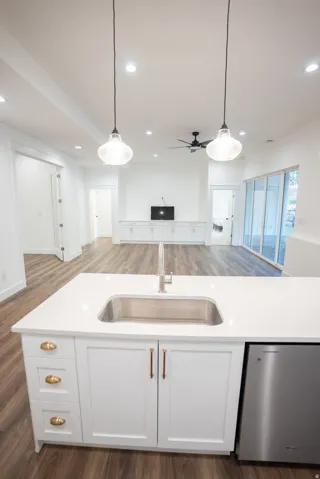 Kitchen island featuring a stainless steel undermount sink, a pull-down faucet, white shaker cabinetry with brass hardware, and a built-in stainless steel dishwasher