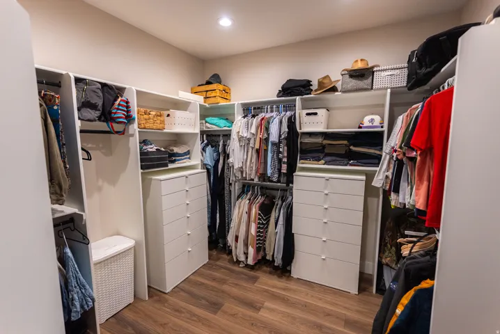 Custom closet system featuring wood-finish flooring, recessed lighting, multiple hanging rods, integrated shelving, and built-in drawer storage