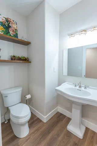 Pedestal sink with chrome fixtures, wood-finish flooring, and white baseboards
