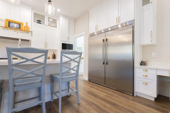 Modern kitchen featuring a large stainless steel refrigerator, white cabinetry with gold-tone hardware, wood-finish flooring, a built-in microwave, and a white countertop