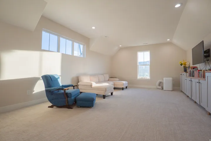 Spacious room featuring sloped ceilings, recessed lighting, carpet flooring, a wall-mounted television, and a built-in cabinetry system with a wood-finish countertop